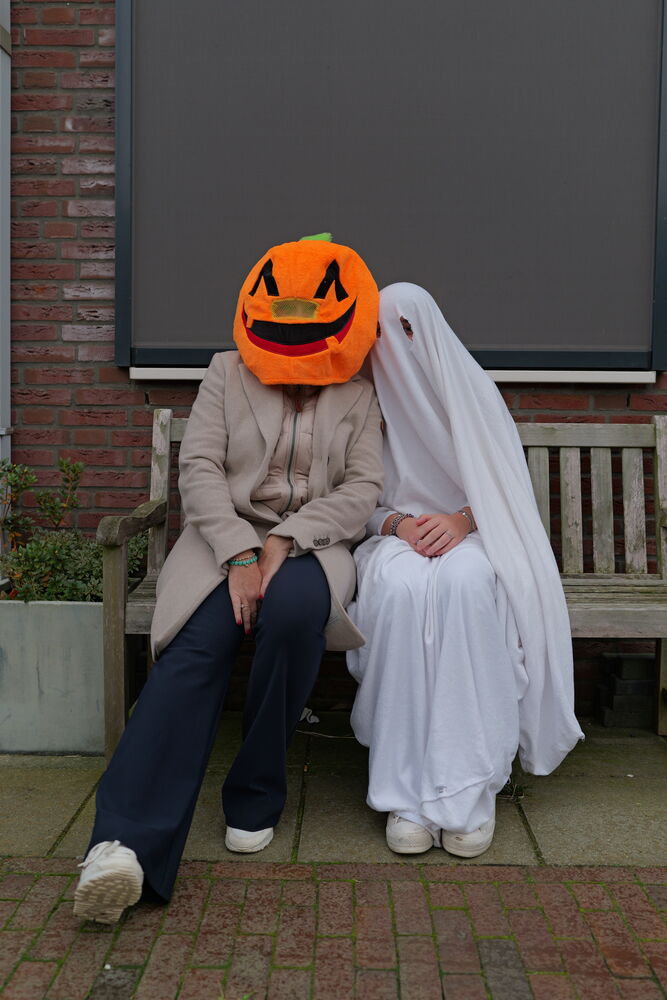 Twee mensen zitten op een bankje, verkleed als spook en pompoen
